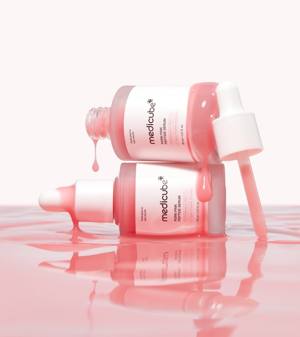 TwoMedicube skincare bottles with pink liquid on a reflective surface
